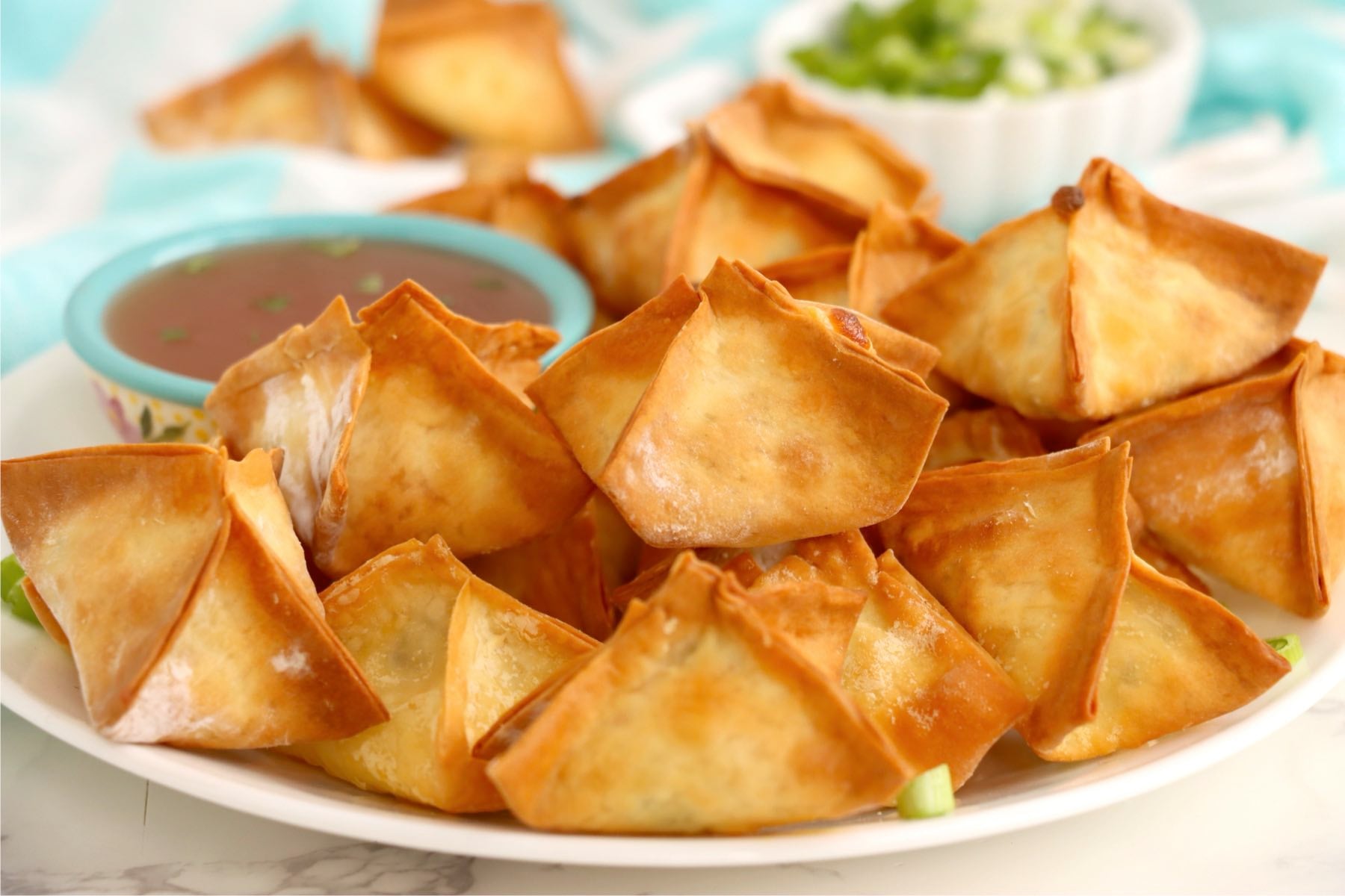 Crispy air fryer crab rangoons arranged around a bowl of dipping sauce.