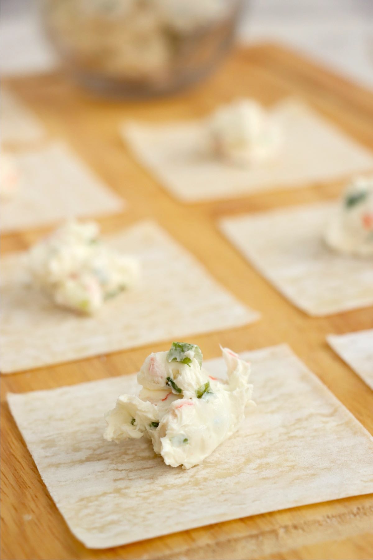 Crab rangoon filling spooned onto a wonton wrapper on a wooden surface.