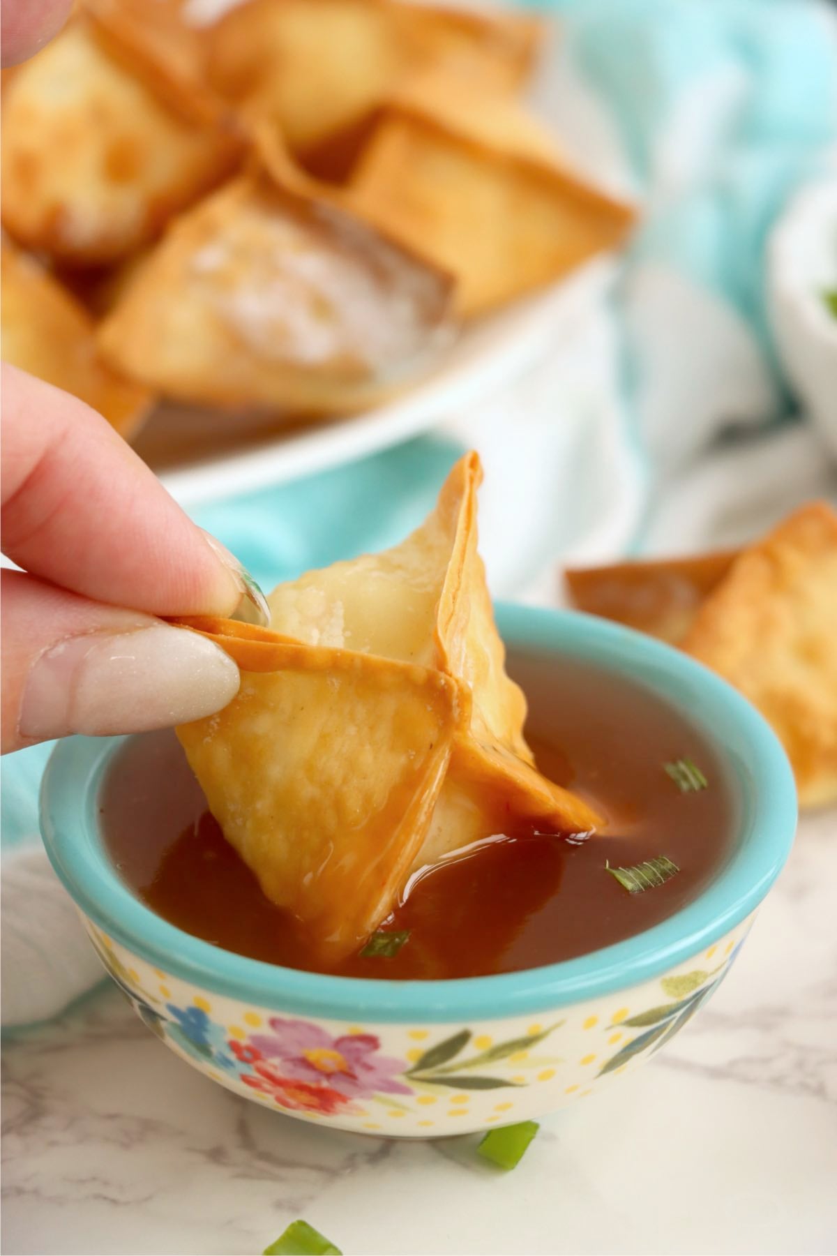 Crab rangoon being dipped into sweet and sour sauce.