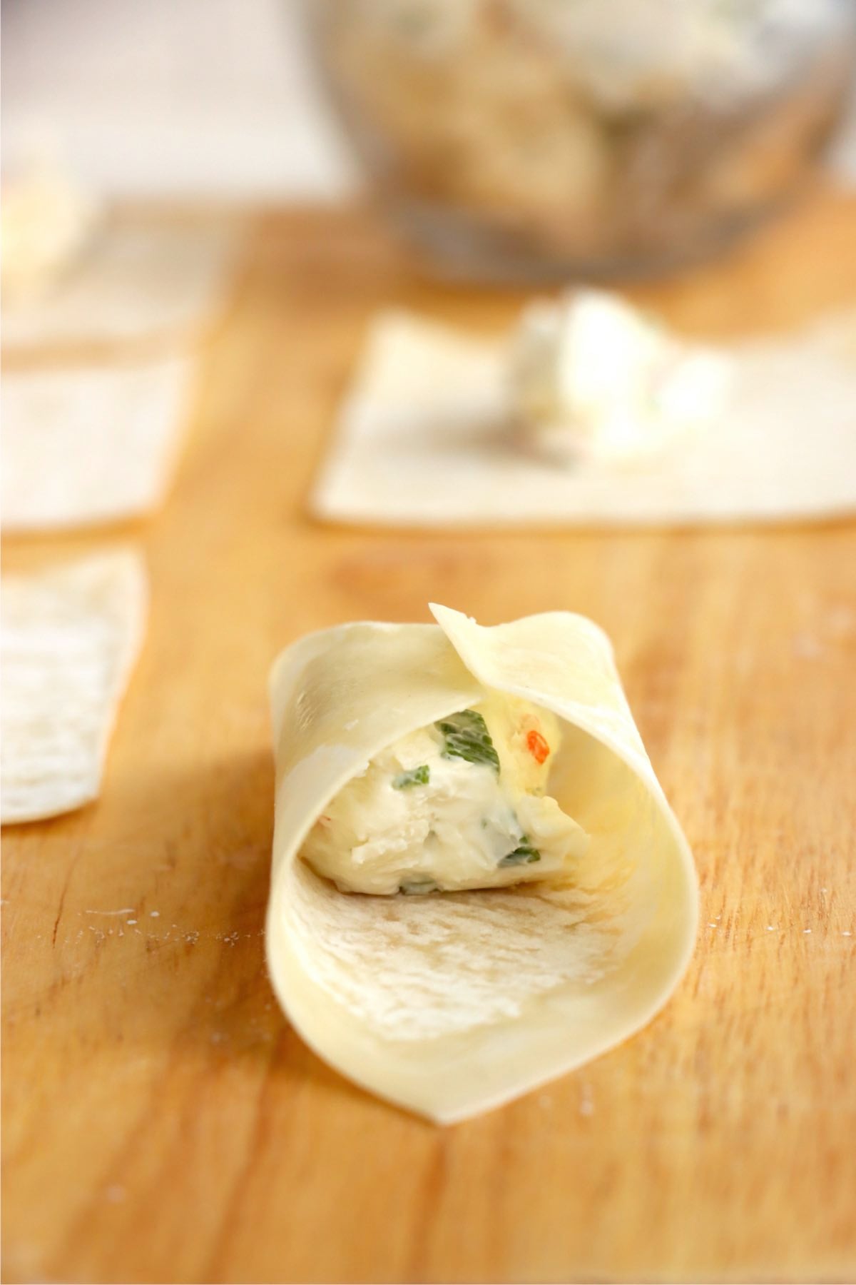Wonton wrapper being folded around crab rangoon filling.
