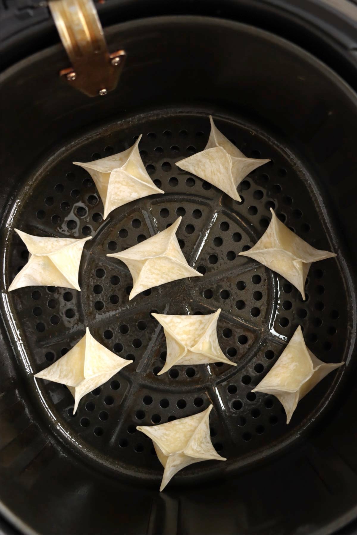 Uncooked crab rangoons arranged in an air fryer basket.