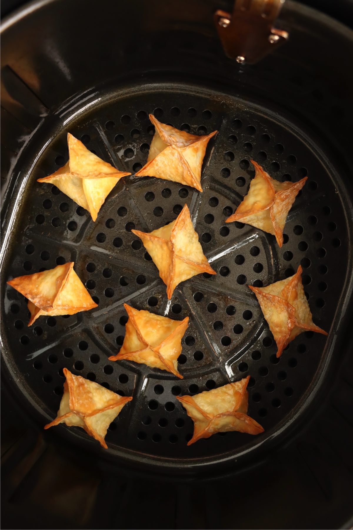 Golden brown crab rangoons cooked in an air fryer basket.