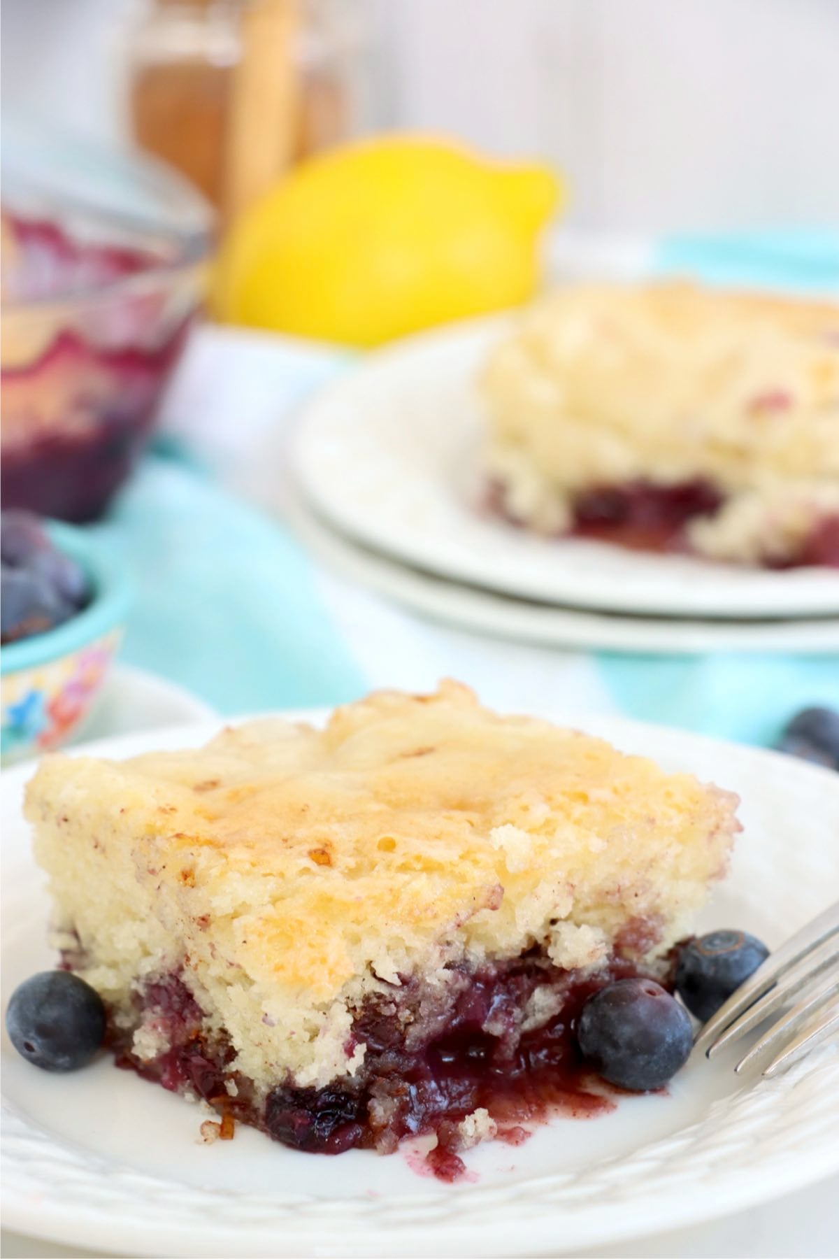 A plated slice of blueberry pudding cake served on a white plate with fresh blueberries.