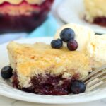 A fork resting beside a slice of blueberry pudding cake with visible blueberry sauce.