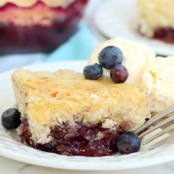 A fork resting beside a slice of blueberry pudding cake with visible blueberry sauce.