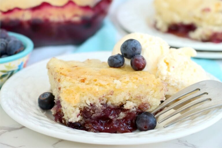 A fork resting beside a slice of blueberry pudding cake with visible blueberry sauce.