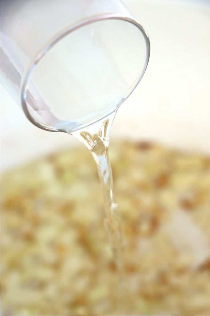 Vodka being poured into sautéed onions to deglaze the pan.