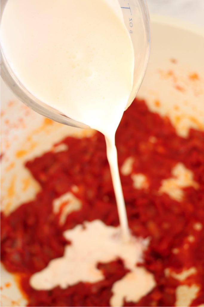 Heavy whipping cream being poured into the tomato vodka sauce.