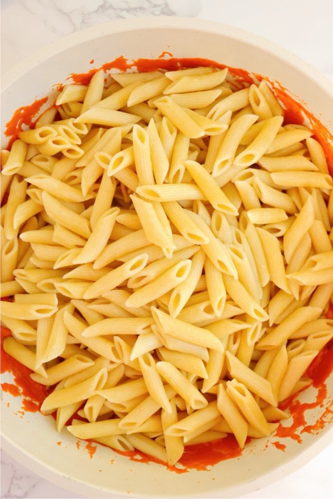 Cooked penne pasta added to the creamy vodka sauce in a skillet.