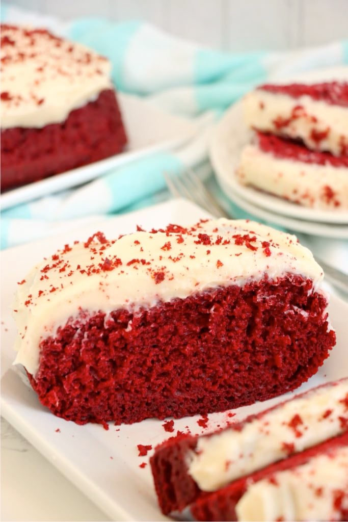 Slice of red velvet loaf cake topped with cream cheese frosting on a white plate.