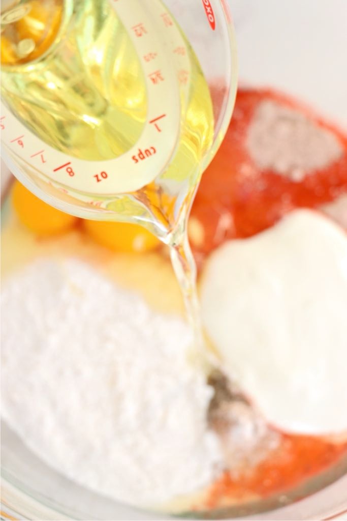 Vegetable oil being poured into a mixing bowl with red velvet cake ingredients.
