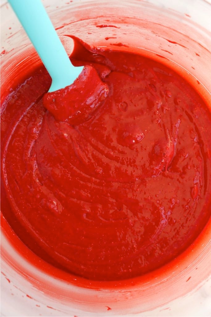 Thick red velvet cake batter being stirred until smooth in a mixing bowl.