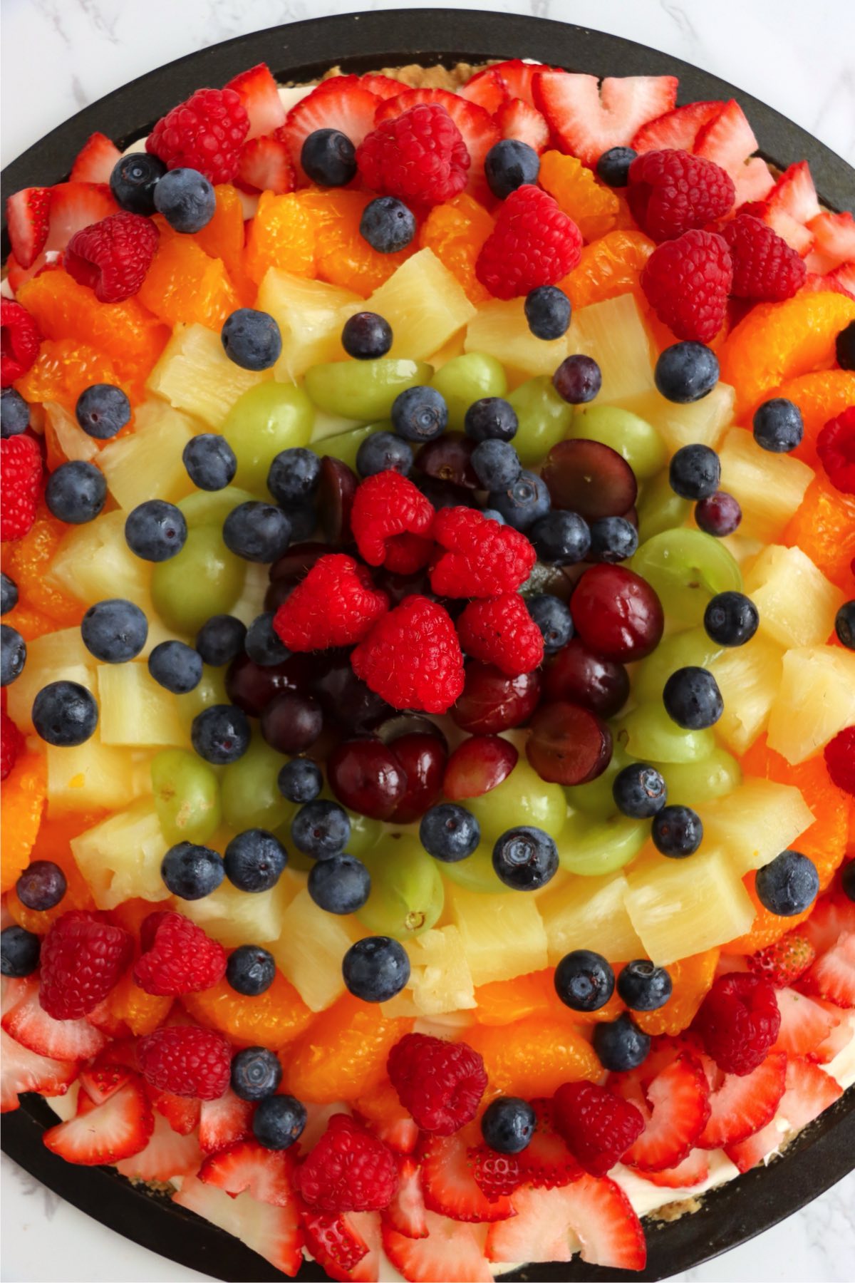 Fresh fruit including strawberries, grapes, pineapple, mandarin oranges, blueberries, and raspberries layered on a tart.