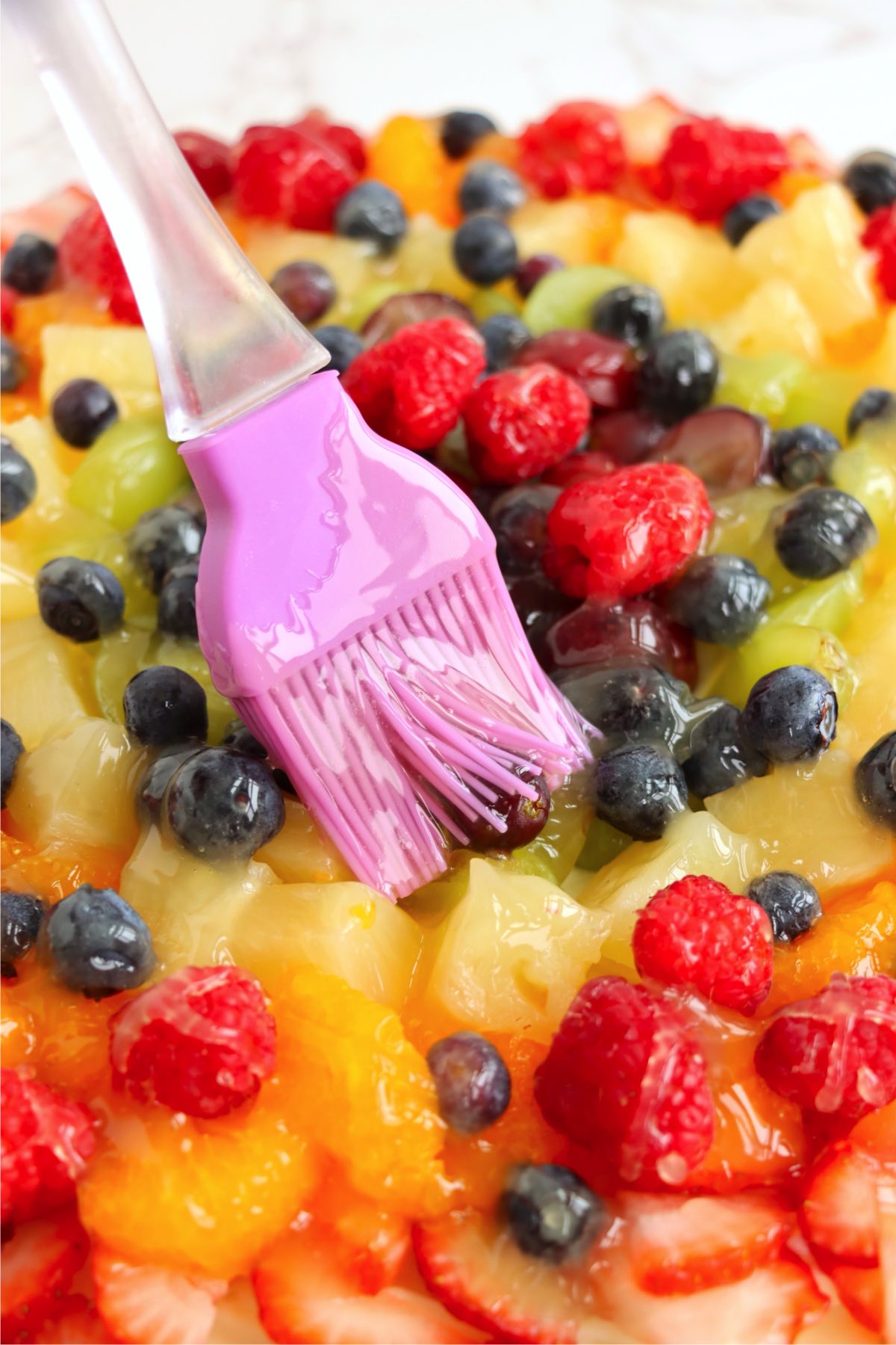 Glaze being brushed over a fresh fruit topping on a dessert tart.
