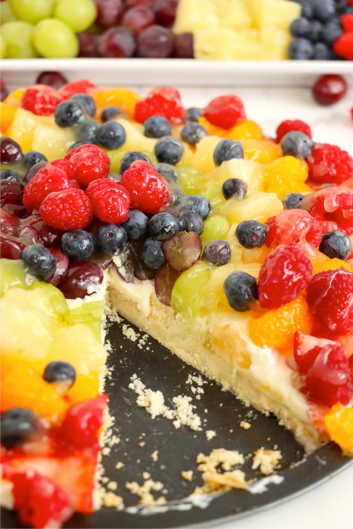 Fruit tart with a slice removed showing the crust and creamy filling layers.