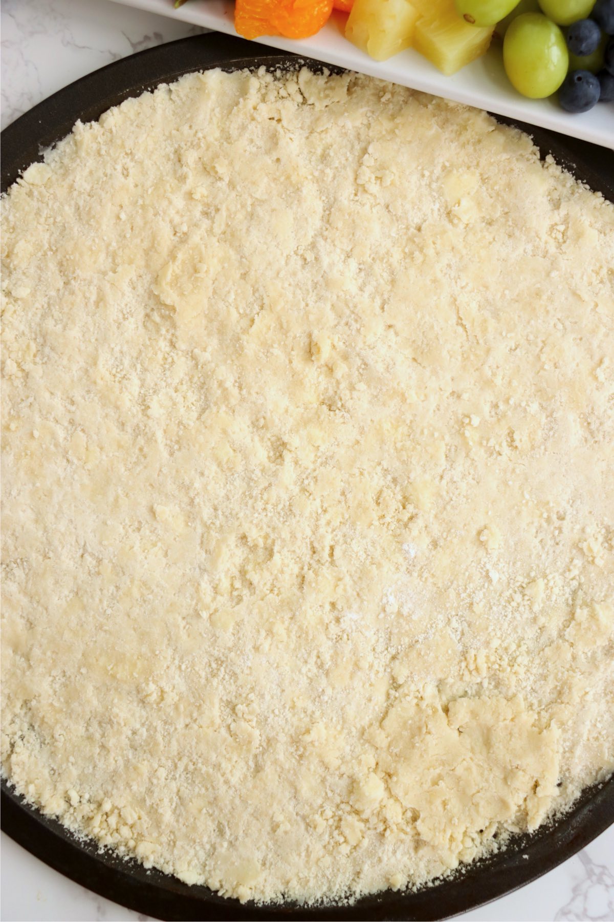 Tart crust dough pressed evenly into a round pizza pan before baking.