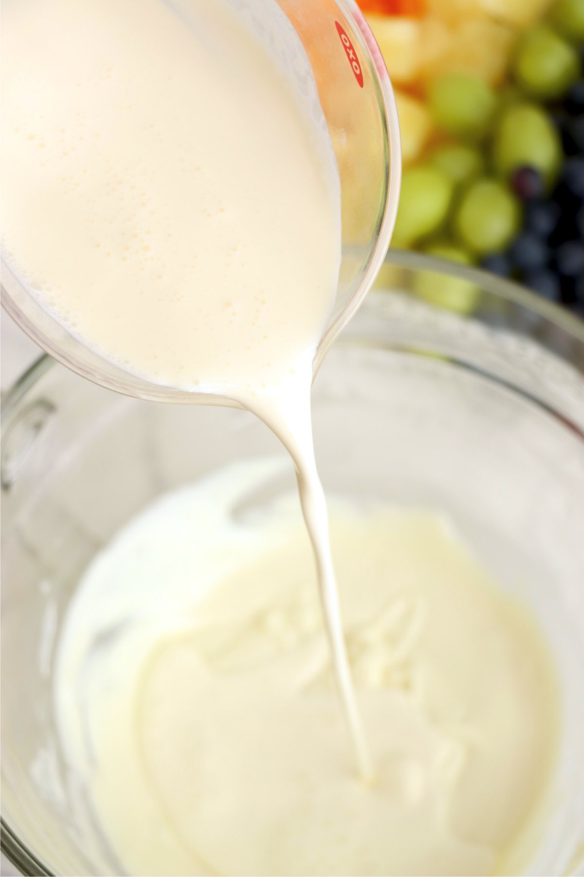 Melted white chocolate combined with cream being poured into a mixing bowl.