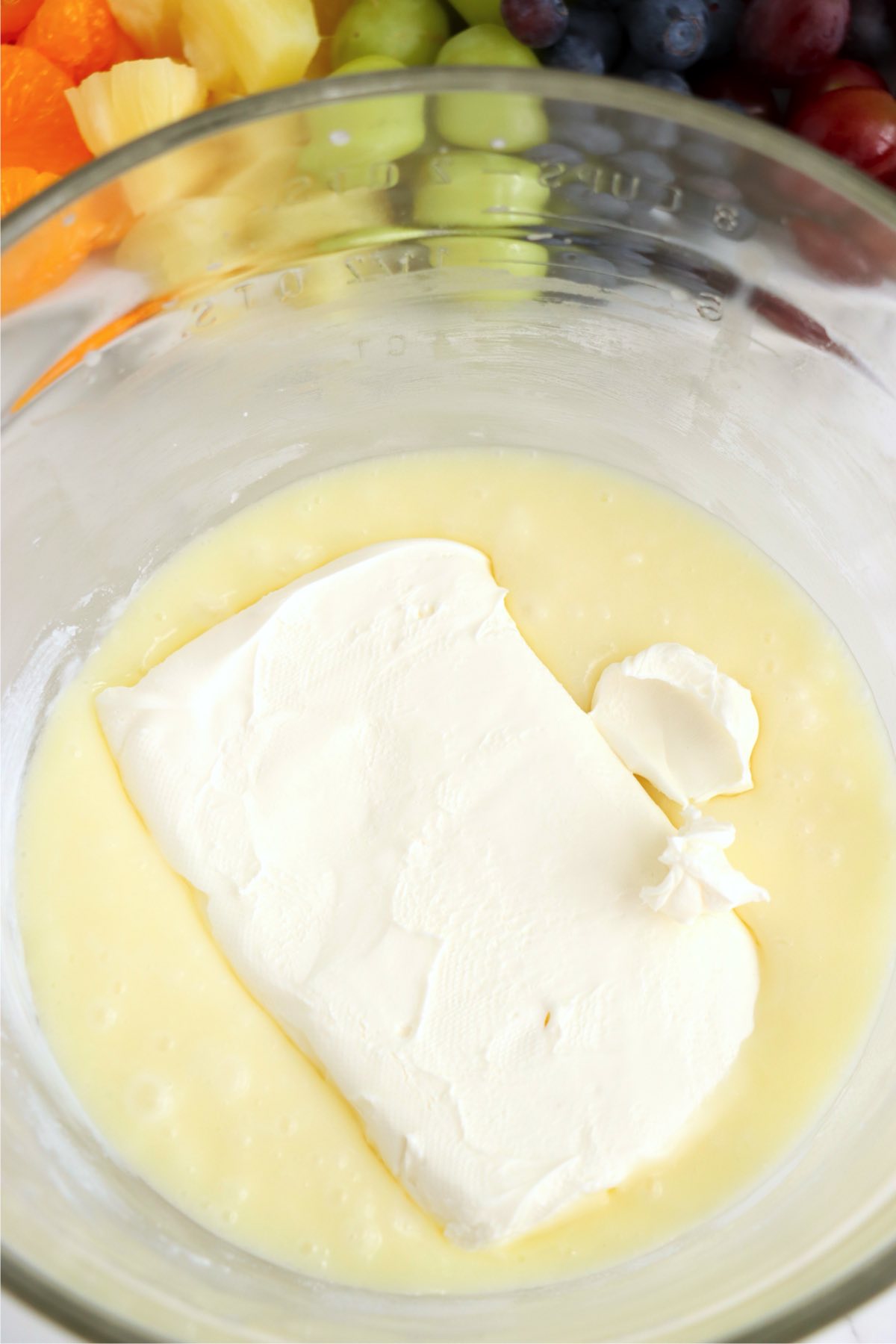 Cream cheese added to the white chocolate mixture in a bowl for the tart filling.