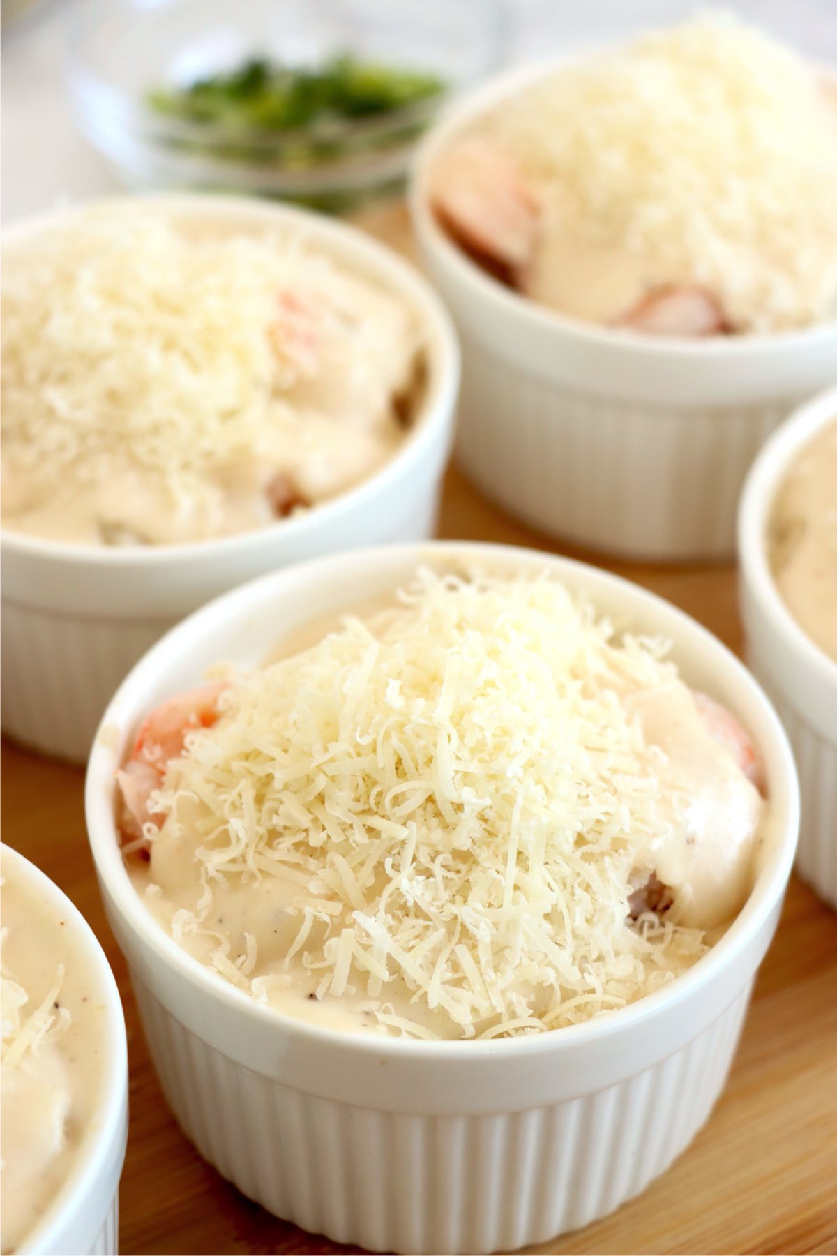 Parmesan cheese sprinkled on top of seafood and sauce in ramekins.