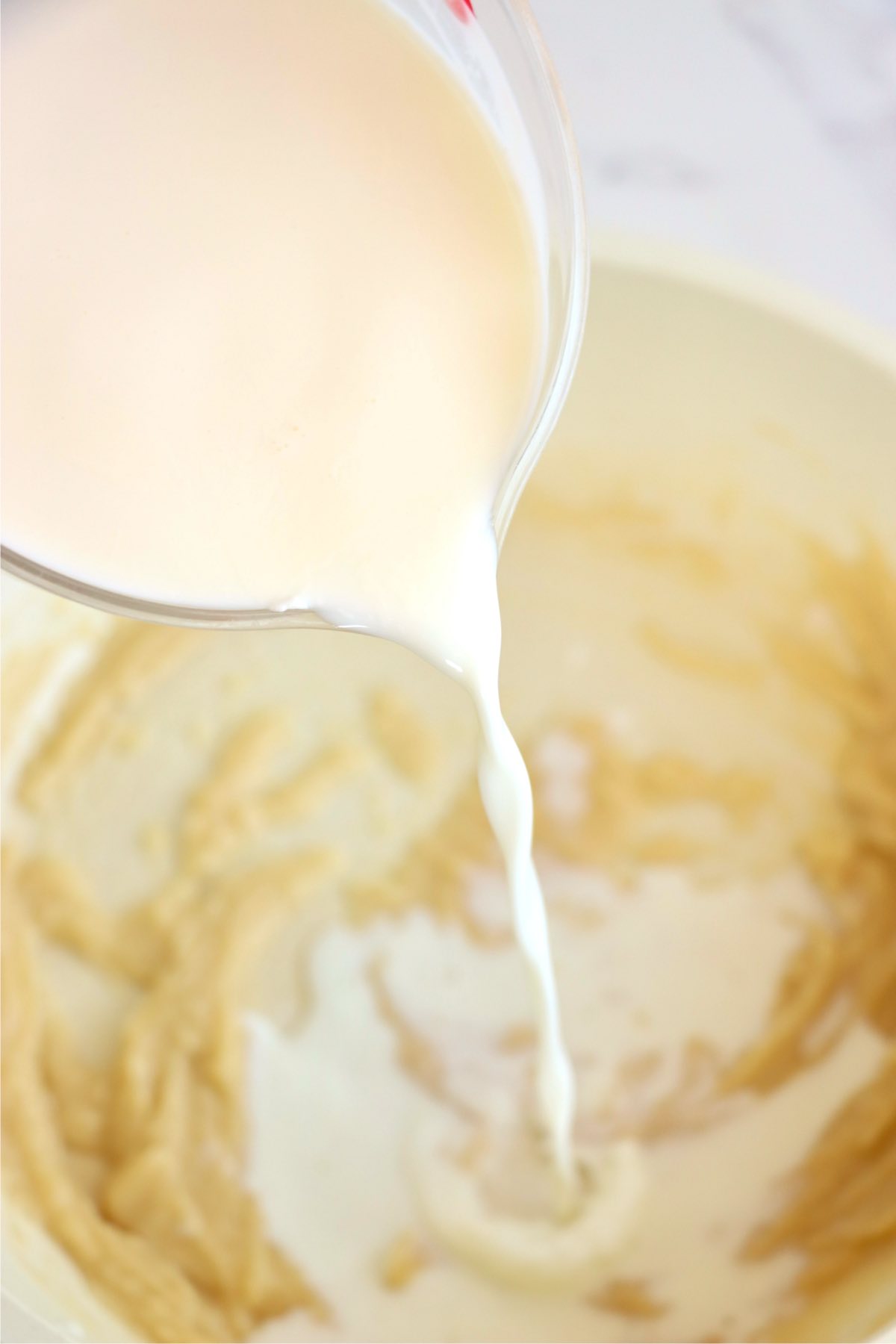 Milk being poured into a roux to create a creamy white sauce for Coquilles St. Jacques.