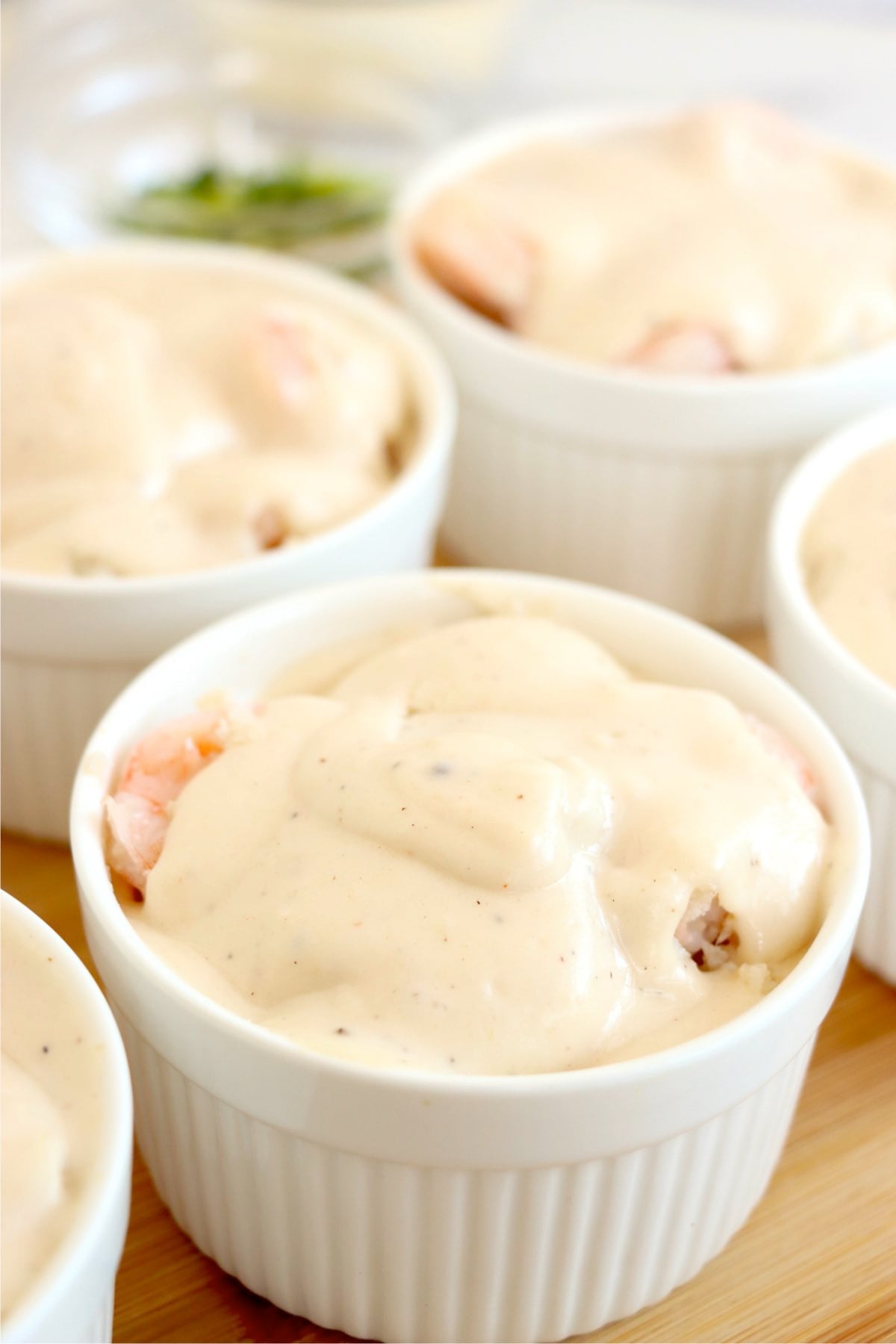 Creamy sauce poured over shrimp and scallops in ramekins before baking.