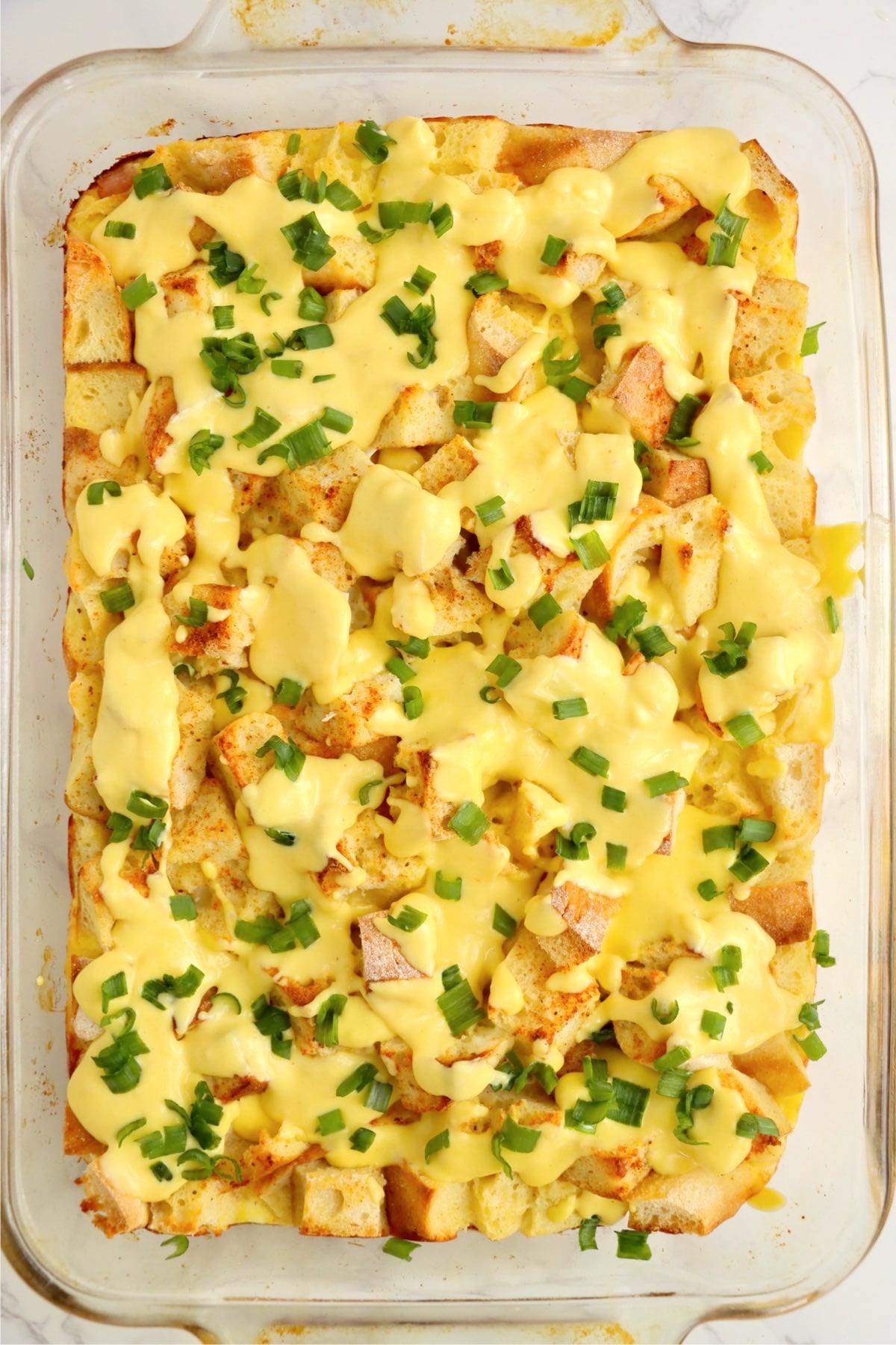 Eggs Benedict casserole topped with hollandaise sauce and minced chives.