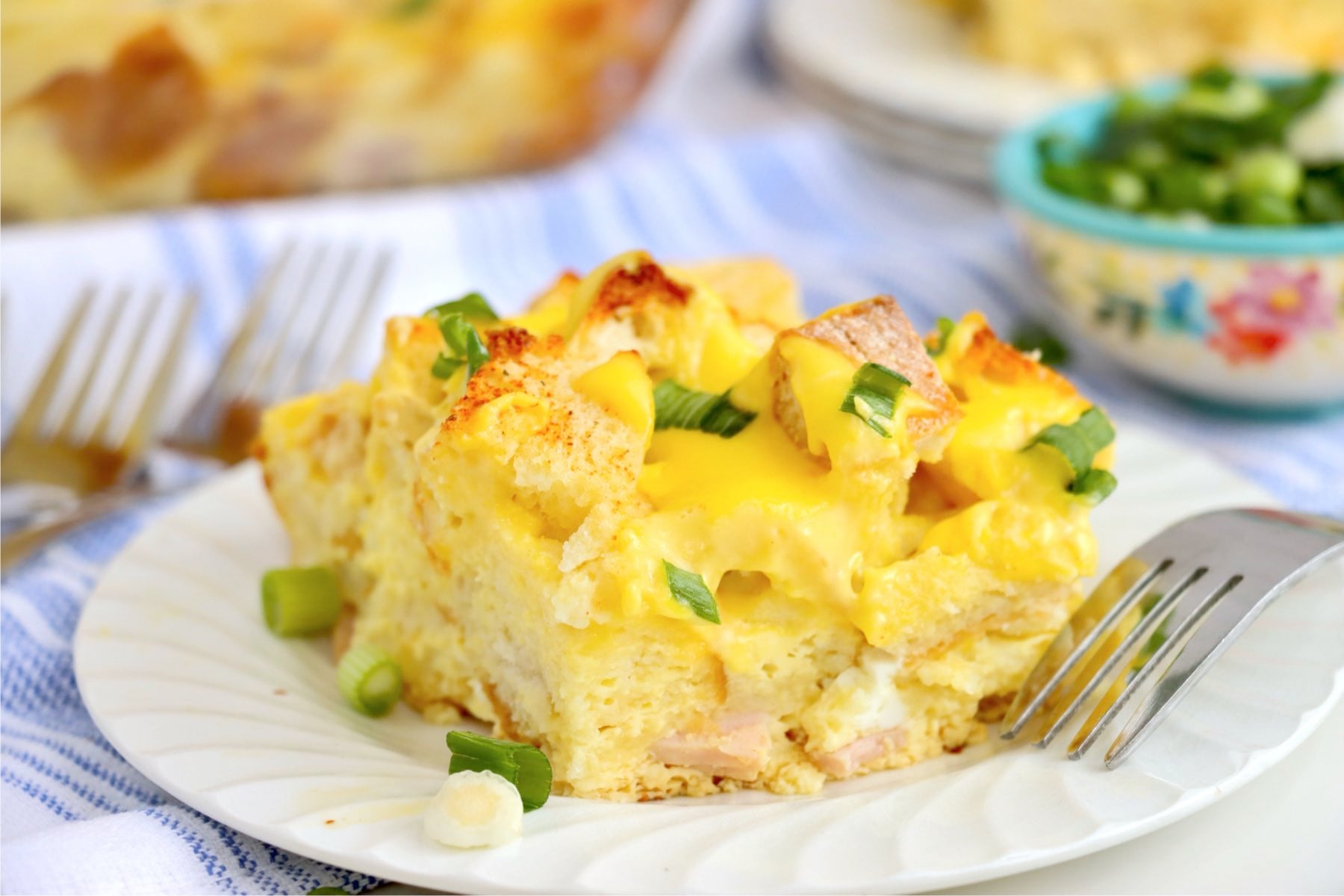 Single serving of eggs Benedict casserole on a white plate with green onions.