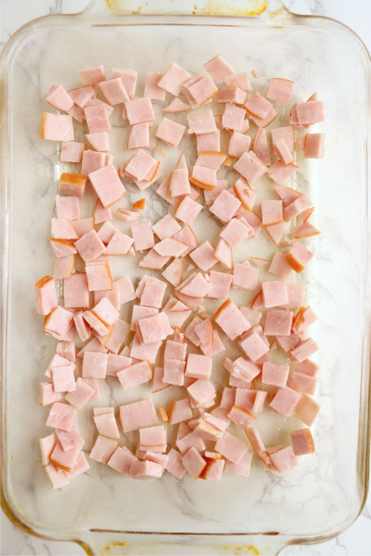 Chopped Canadian bacon spread in the bottom of a glass baking dish.