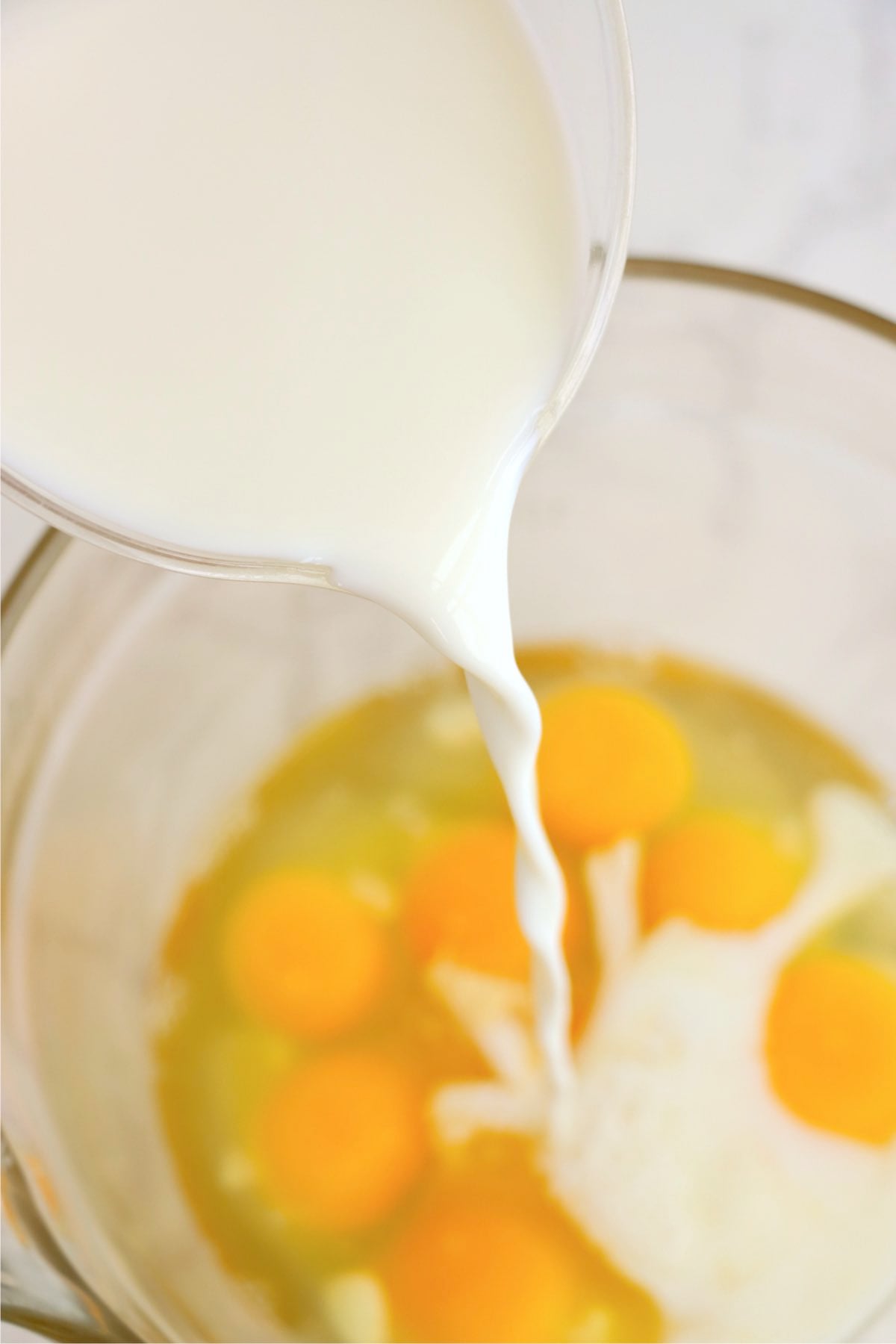 Milk being poured into a bowl of eggs for a casserole mixture.