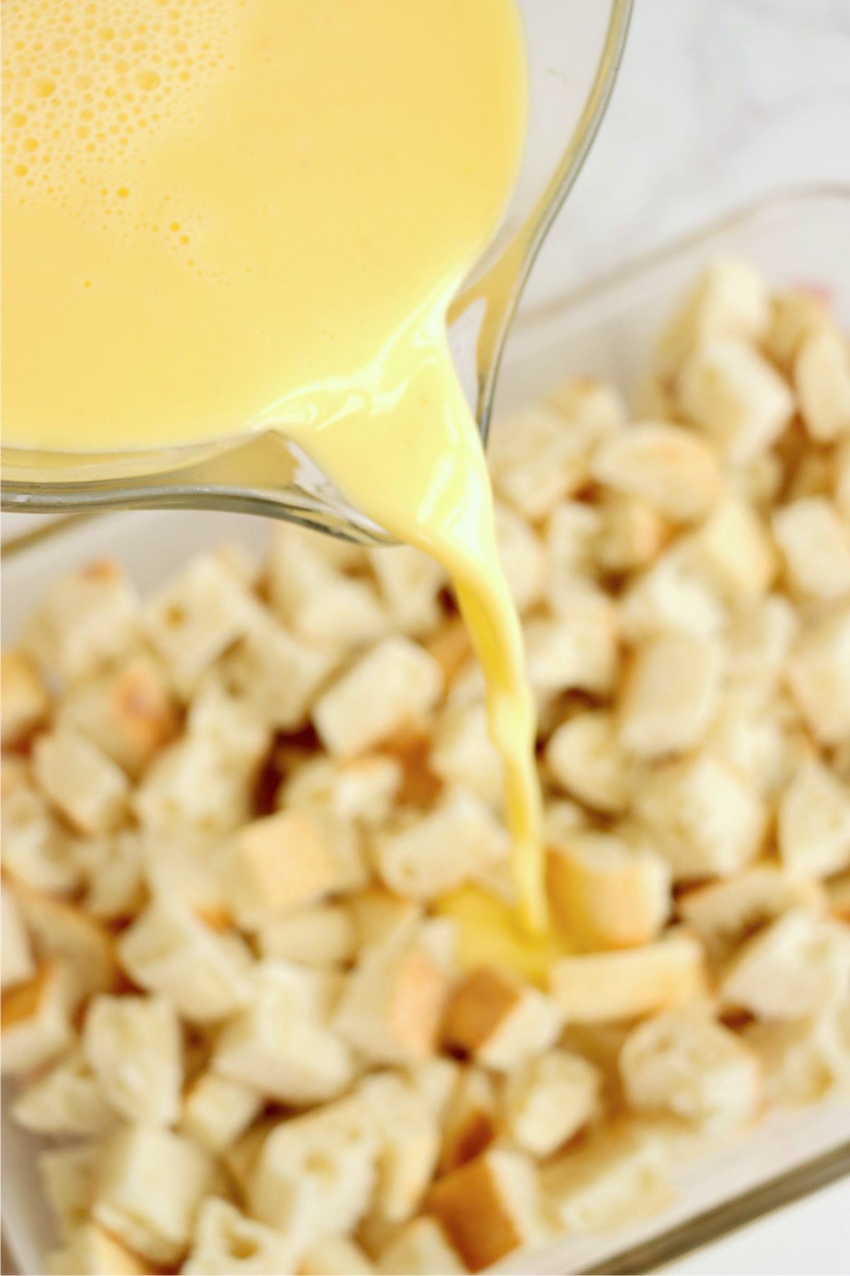 Egg mixture being poured over English muffins in a baking dish.