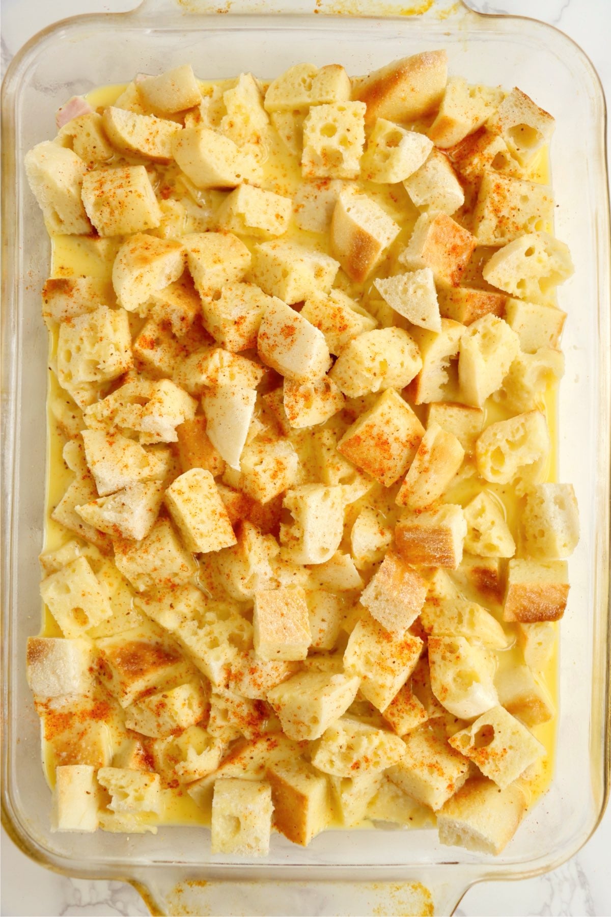 Paprika sprinkled over unbaked eggs Benedict casserole.