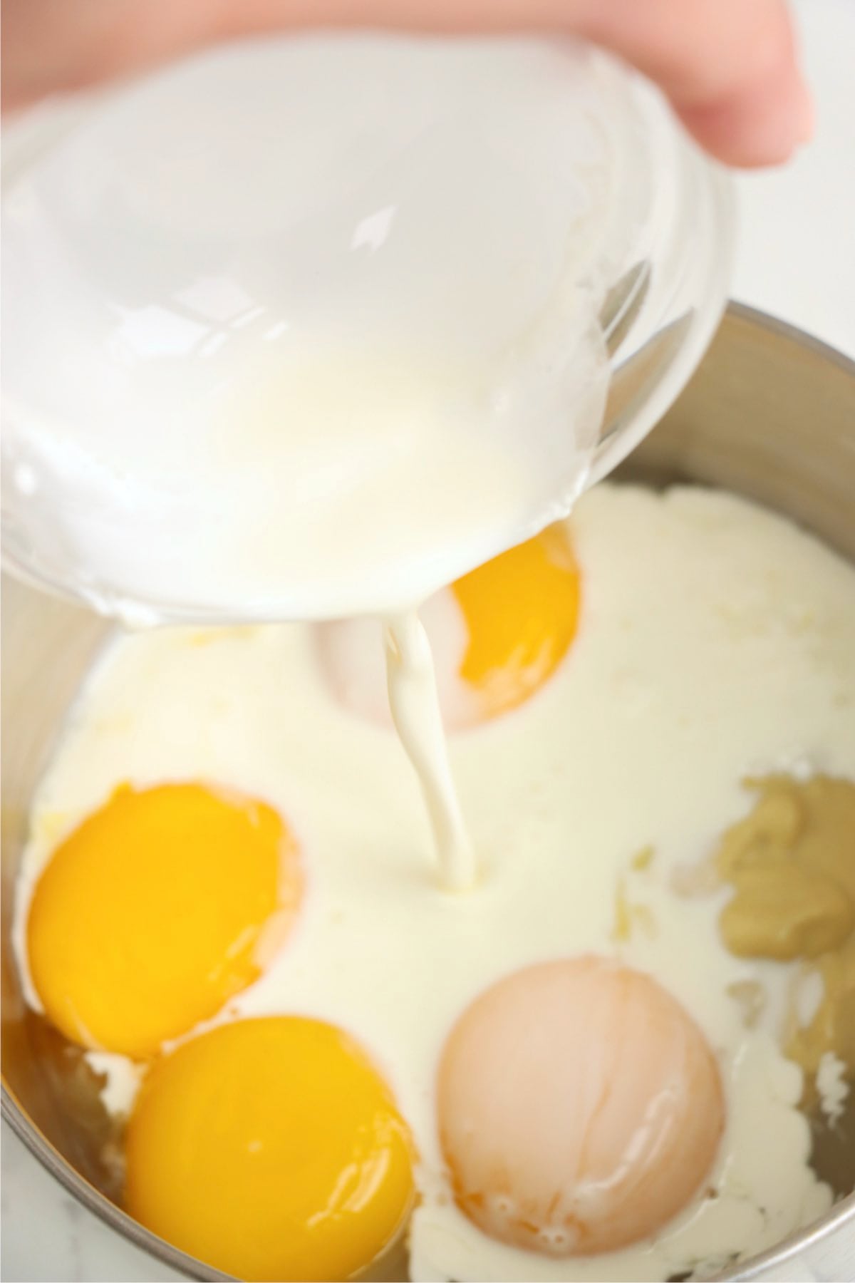 Heavy cream being poured into egg yolks and Dijon mustard to make hollandaise sauce.