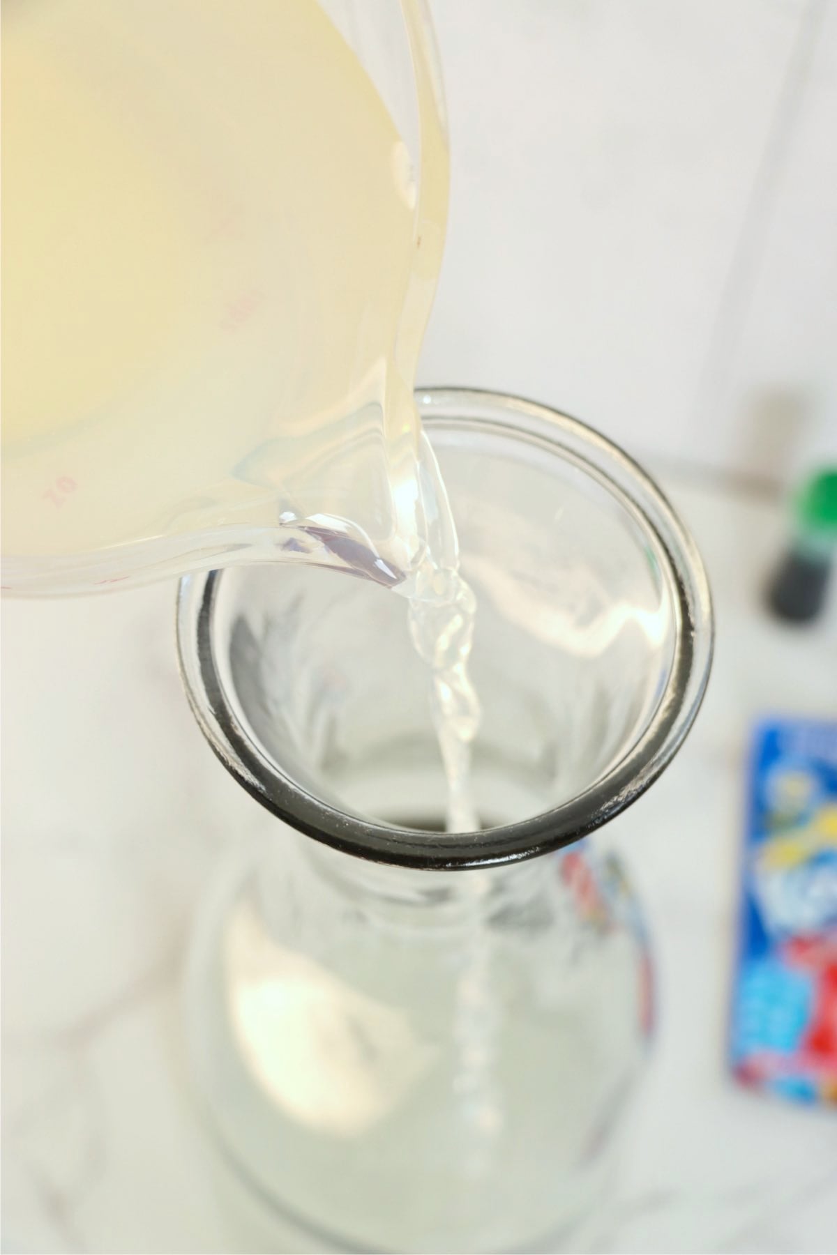 Lemonade being poured from a measuring cup into a clear glass pitcher.