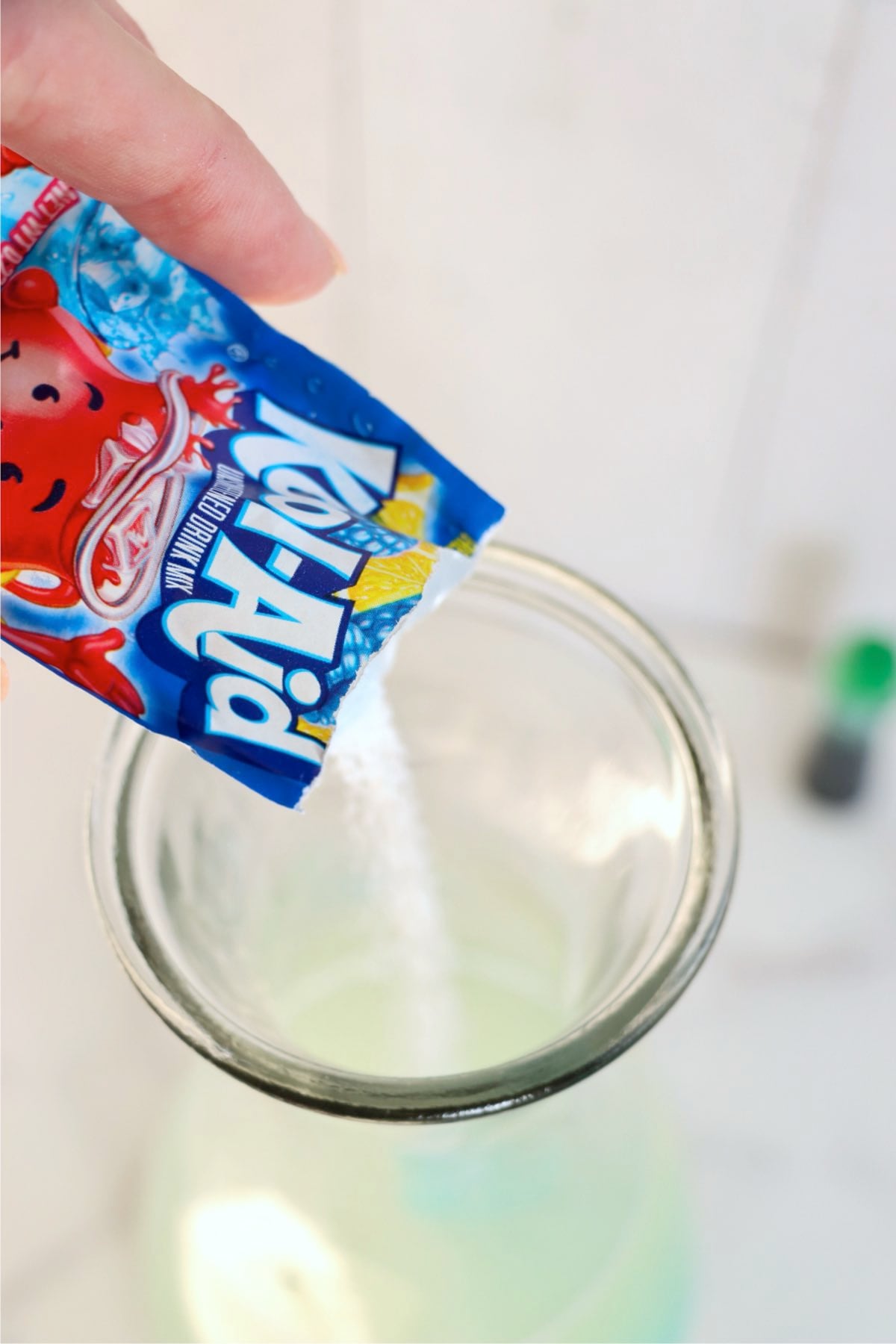 Blue raspberry drink mix being poured into a glass pitcher.