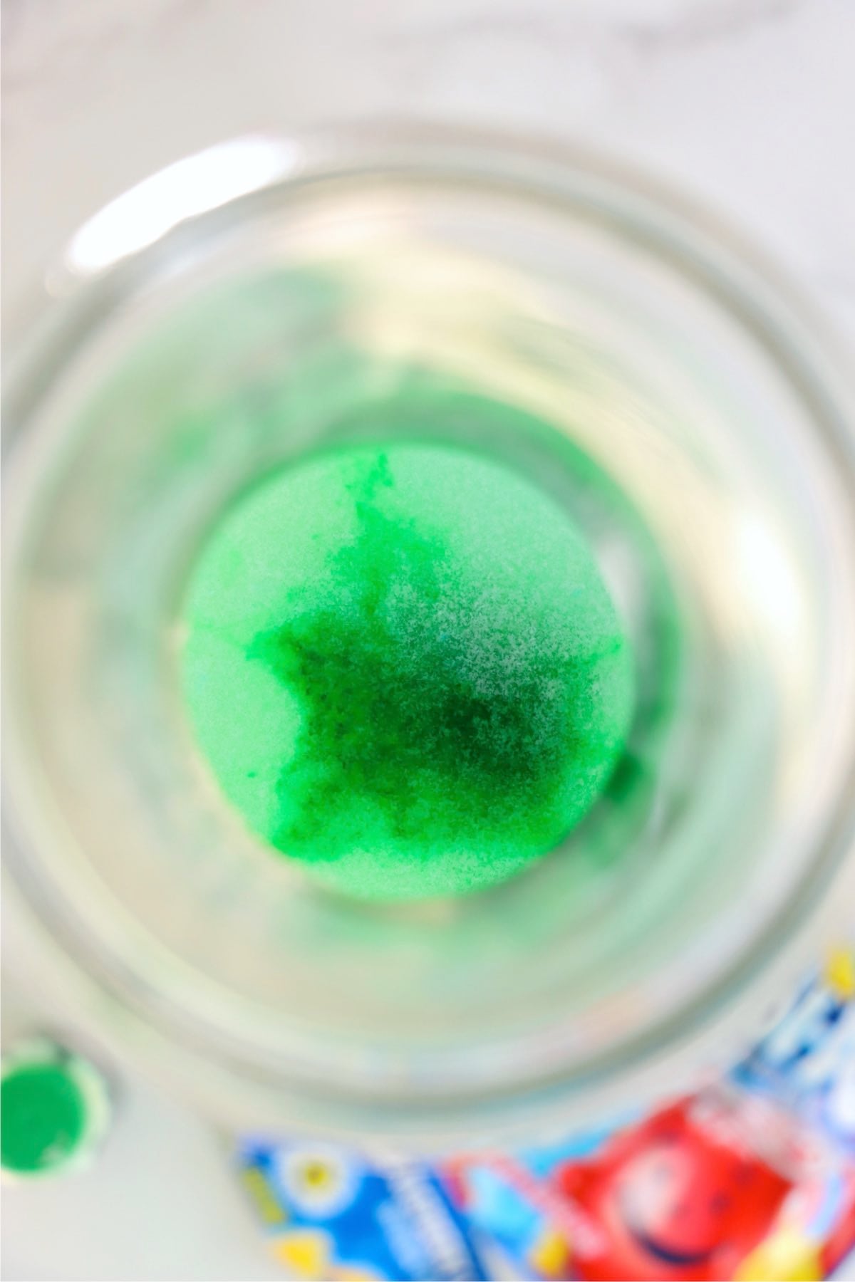 Top view inside a pitcher showing drink mix and green food coloring beginning to blend with lemonade.
