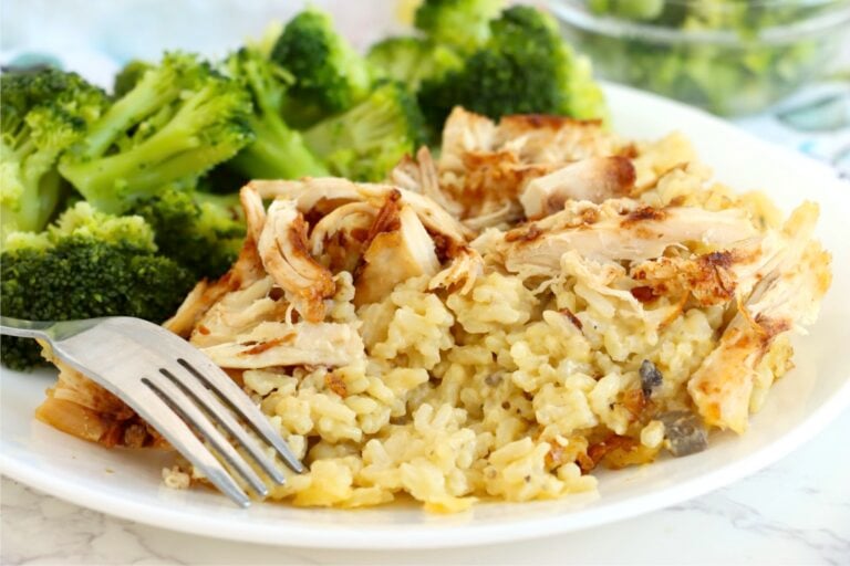 Creamy chicken and rice casserole served on a white plate with steamed broccoli and casserole dish in the background.