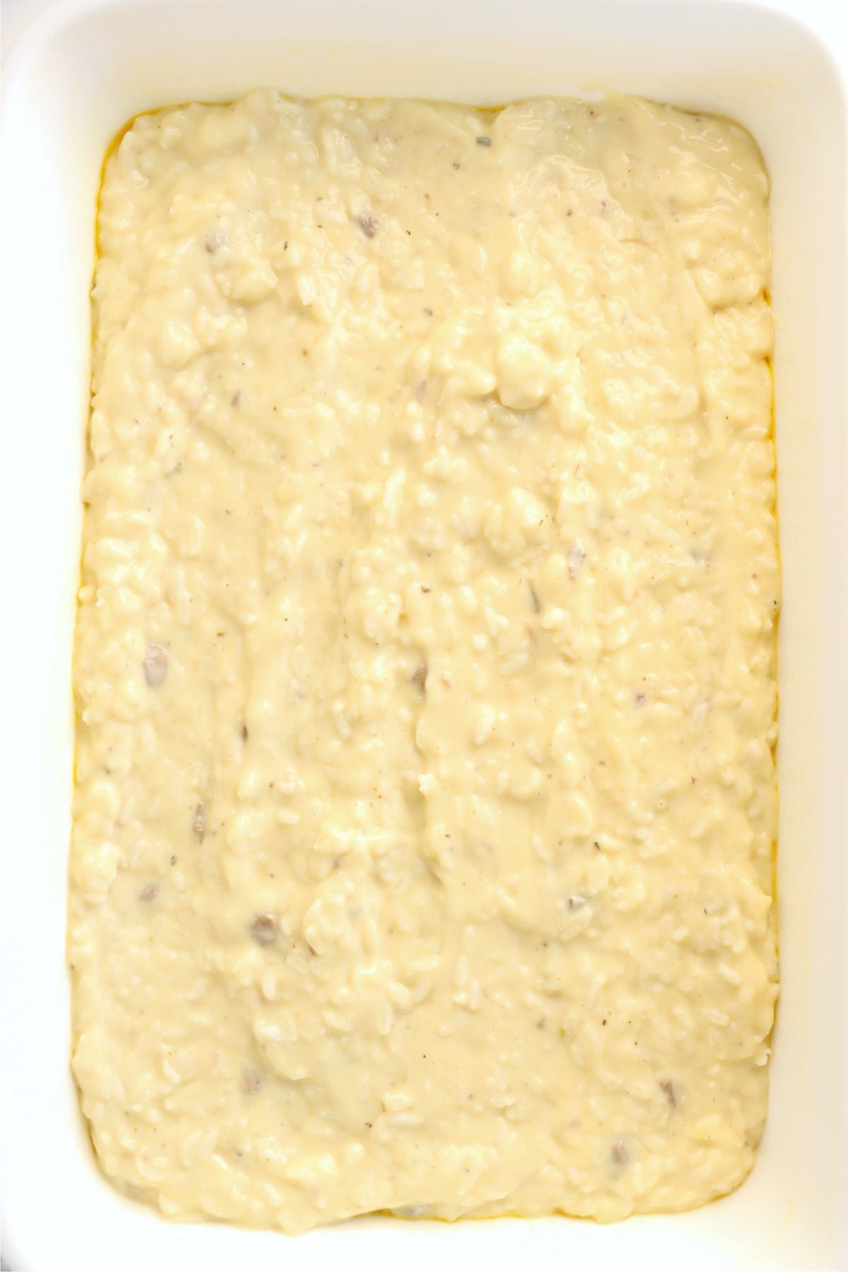 Uncooked rice mixed with cream of chicken and cream of mushroom soups spread evenly in a white baking dish.