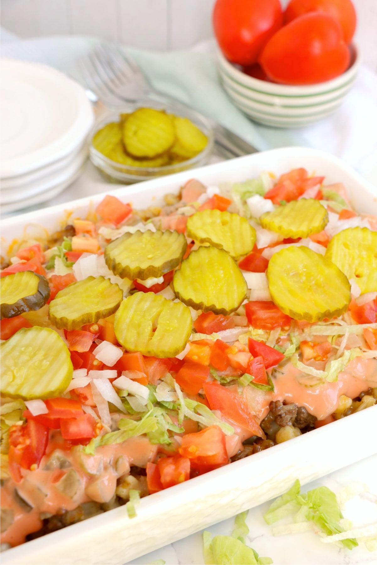 Finished casserole topped with lettuce, tomatoes, pickles, and sauce.
