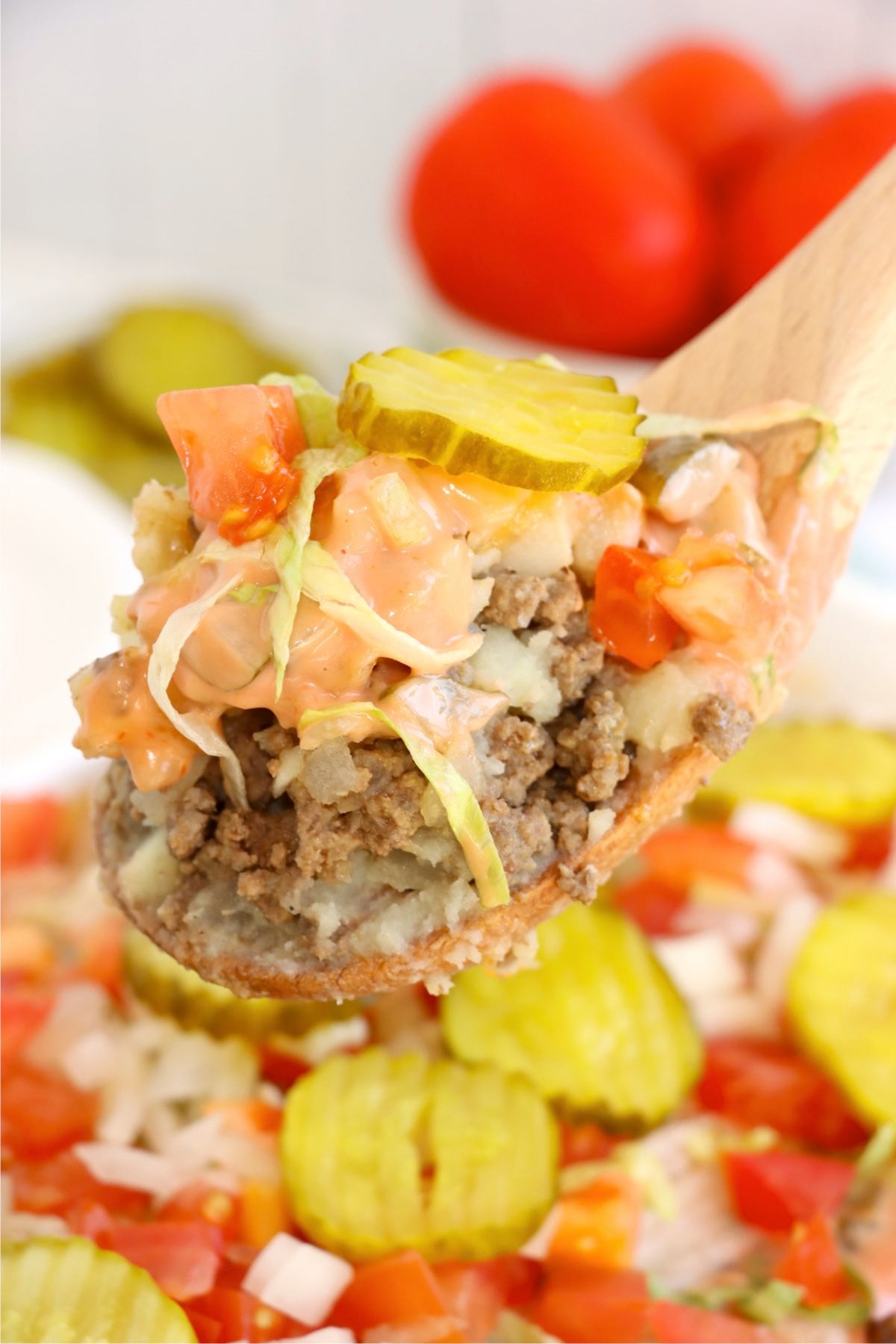 Spoonful of Big Mac casserole showing layers of beef, potatoes, and toppings.