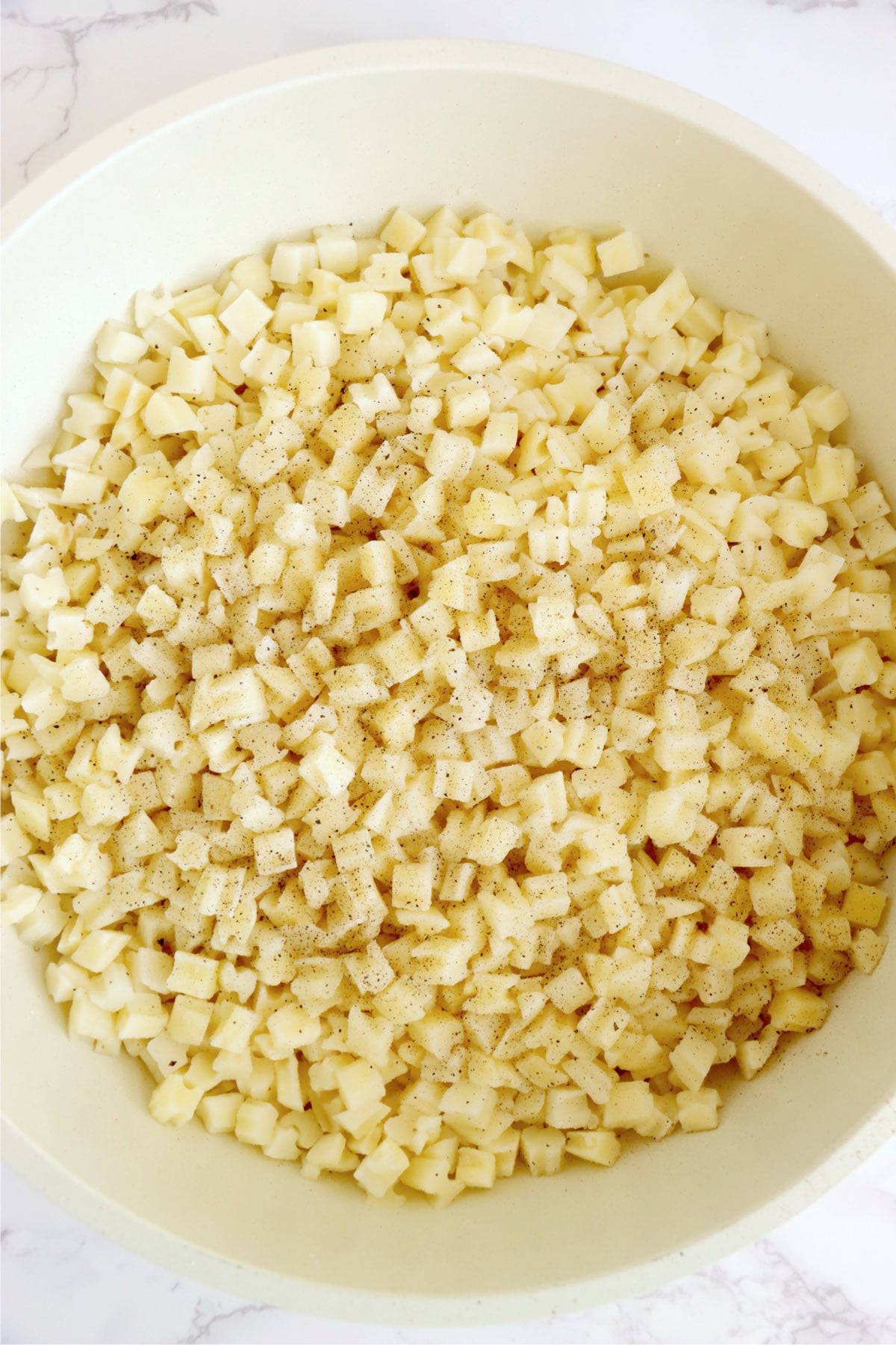 Diced hash browns cooking in a skillet with seasoning.