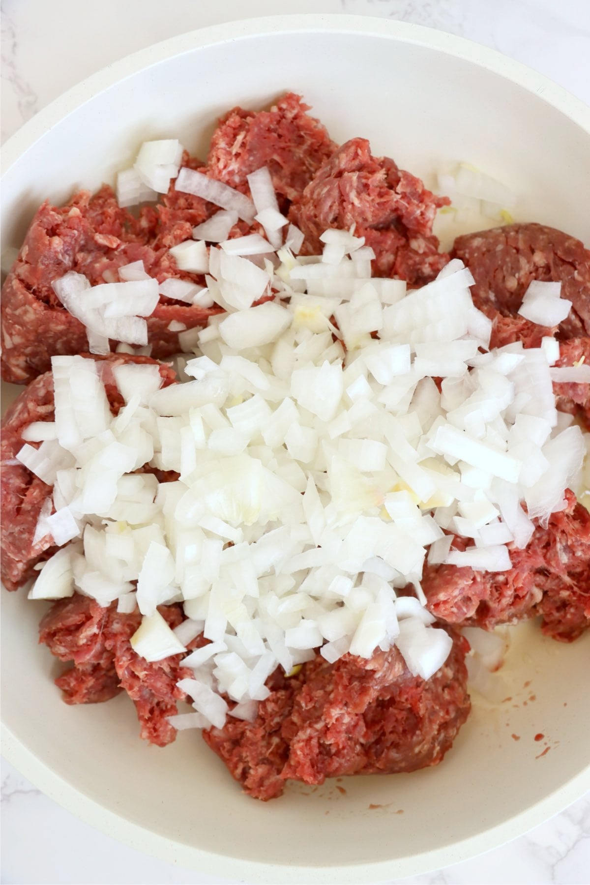 Raw ground beef and diced onions in a skillet before cooking.