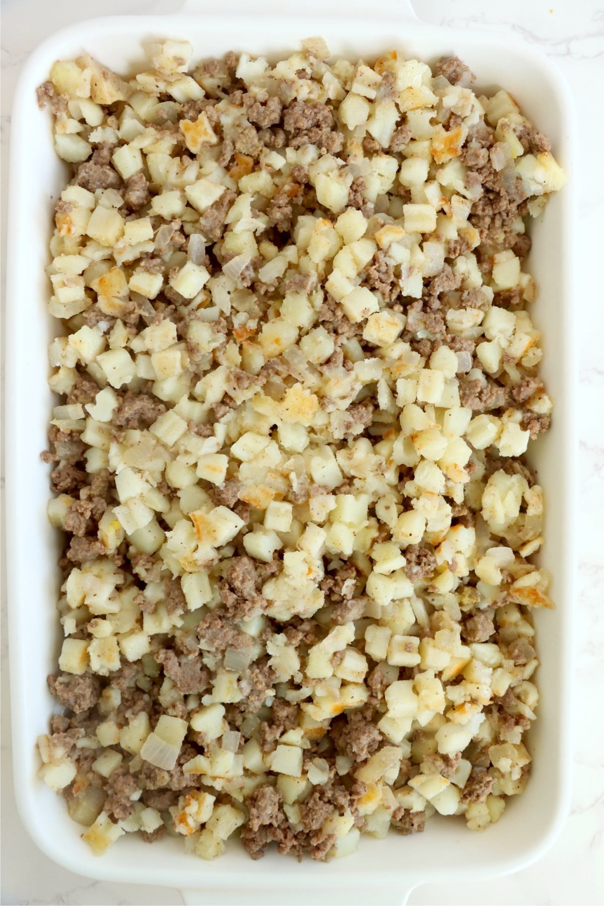 Beef and hash brown mixture combined in a baking dish.