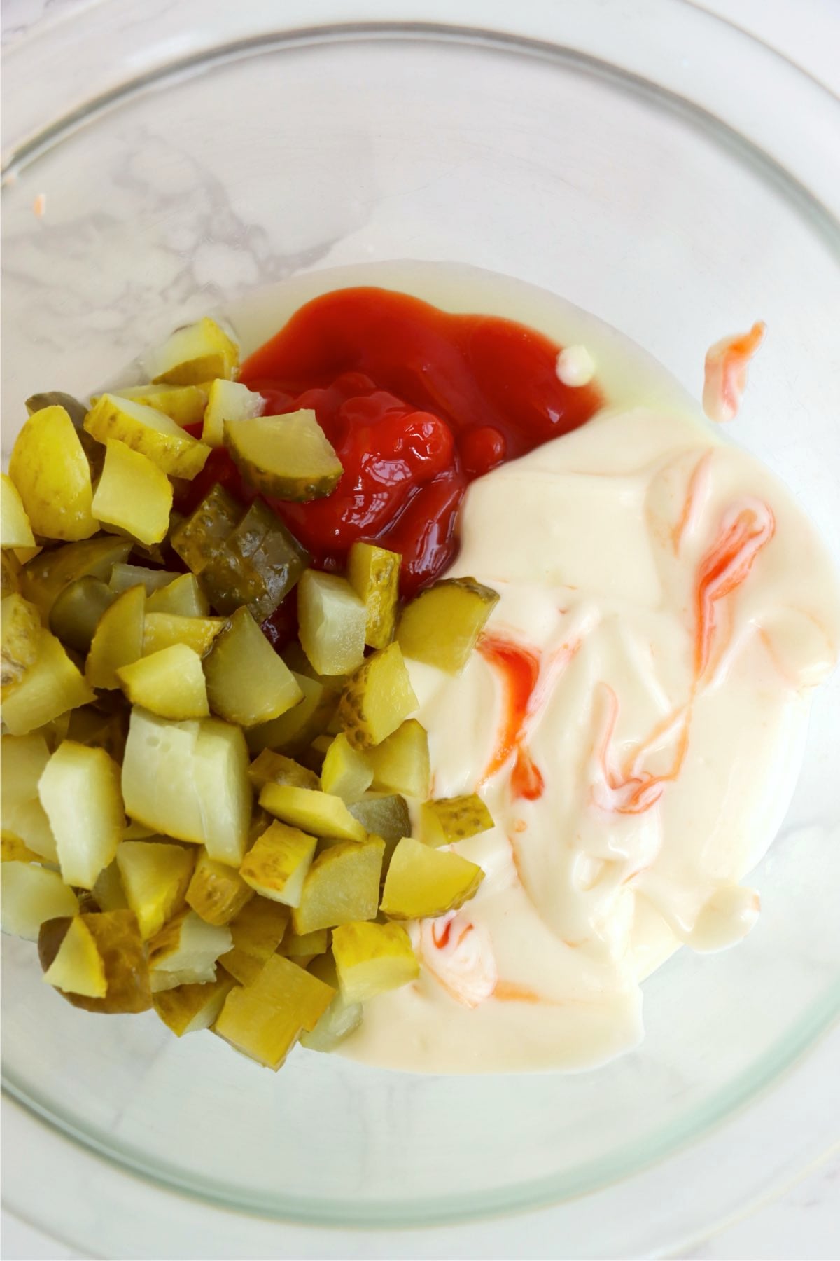 Glass bowl filled with ketchup, mayo and chopped pickles.