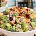Bowl of broccoli crunch salad with apples, shredded carrots, red onion, cranberries, and walnuts.