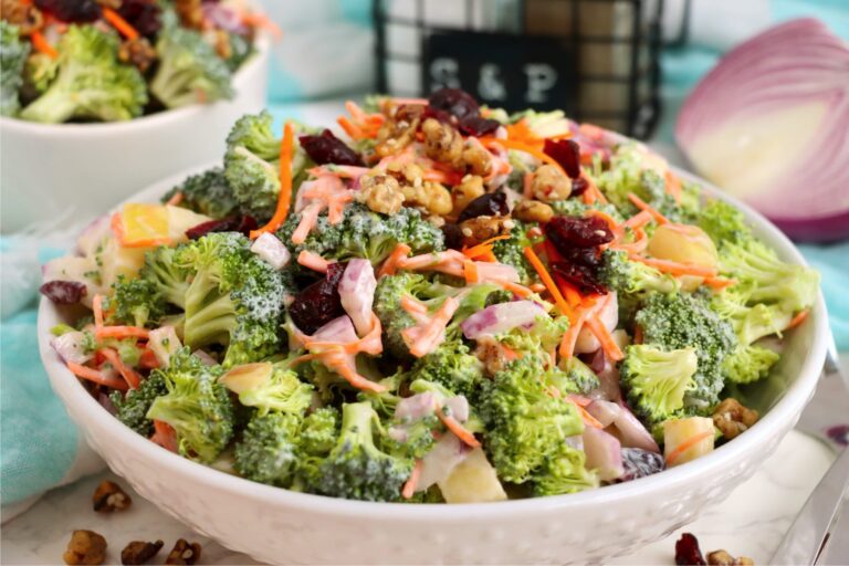 Bowl of broccoli crunch salad with apples, shredded carrots, red onion, cranberries, and walnuts.