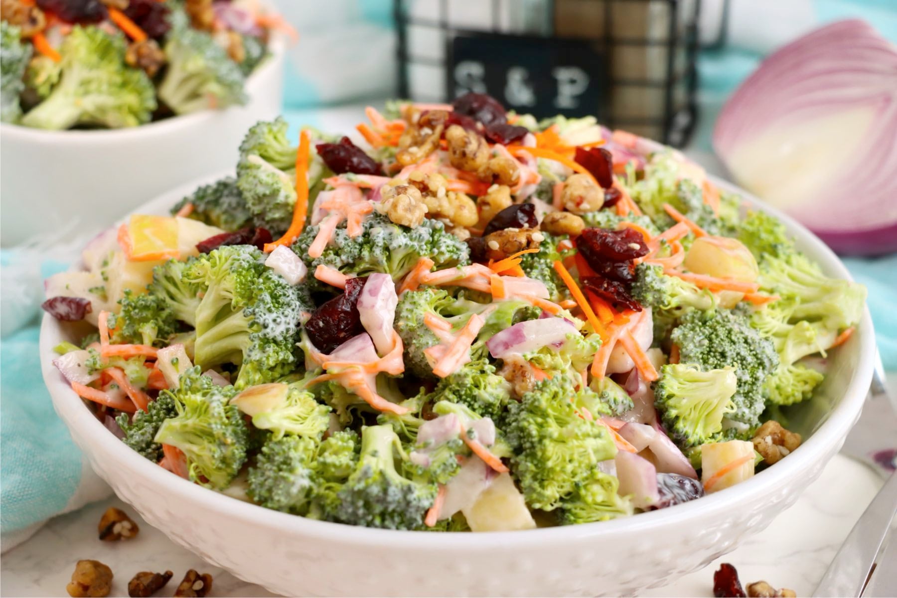 Bowl of broccoli crunch salad with apples, shredded carrots, red onion, cranberries, and walnuts.