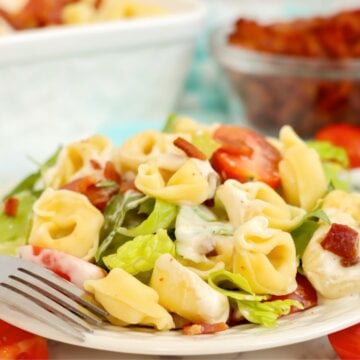 Plated serving of cold tortellini salad with bacon, lettuce, grape tomatoes, and creamy ranch dressing.