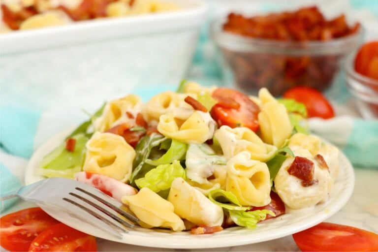 Plated serving of cold tortellini salad with bacon, lettuce, grape tomatoes, and creamy ranch dressing.