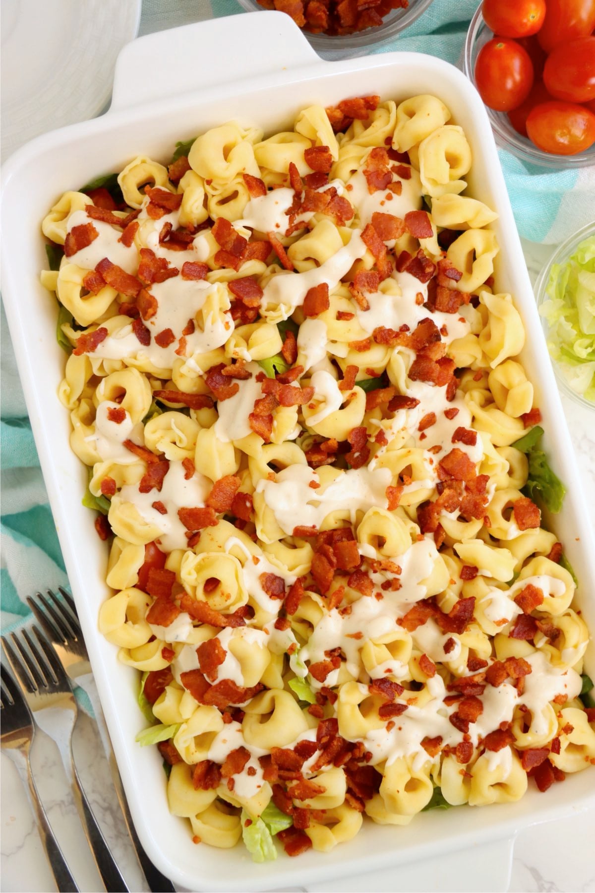 Cold tortellini salad topped with creamy ranch dressing and crispy bacon in a white serving dish.
