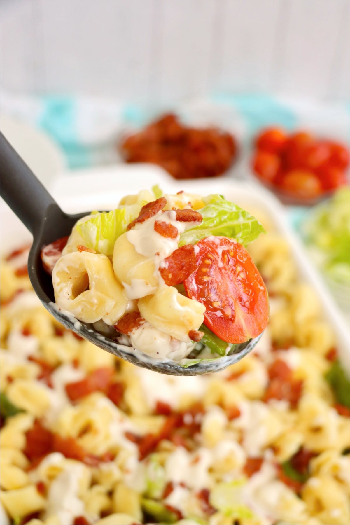 Serving spoon filled with cheese tortellini salad, crispy bacon, ranch dressing, and fresh vegetables.